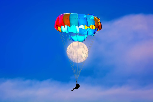 Parachutist on a multi-colored parachute . Full Moon on background - Foto, afbeelding