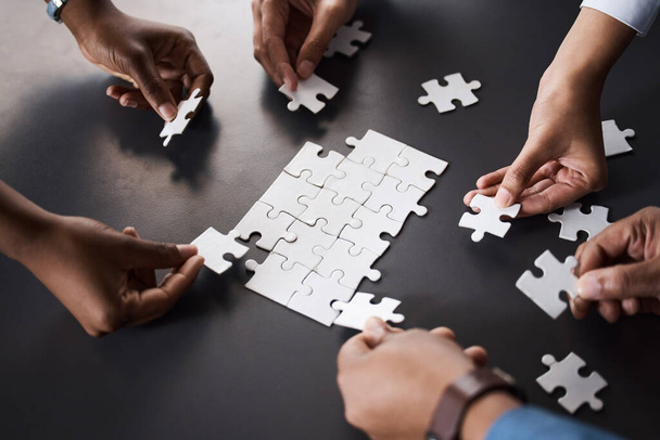 Closeup shot of a group of unrecognisable businesspeople joining puzzle pieces together in an office. - Photo, Image