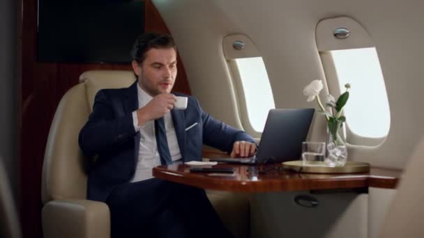Le directeur financier prend une gorgée de café en voyage d'affaires. Patron confiant travail ordinateur portable vérifier les statistiques de vente marketing sur le jet privé de luxe. Focalisé élégant homme regardant avion fenêtre boisson à boire - Séquence, vidéo