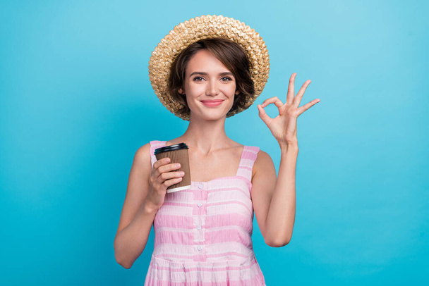 Photo of crazy young fancy lady hold coffee show okey wear hat pink dress isolated on blue color background. - Foto, Imagen