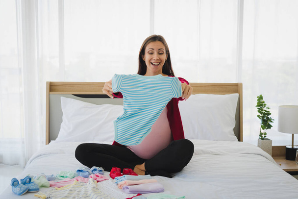 妊娠中の女性でカジュアル服計画と準備彼または彼女の子供服のために彼らの未来で現代の寝室. - 写真・画像