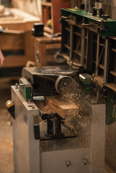 Vertikální záběr části tesařského ocelového řezacího nože, bruska házející dřevěné holicí štěpky, piliny ve vzduchu v tesařské kanceláři, garáži nebo dílně. Výroba nábytku podnikání. - Fotografie, Obrázek