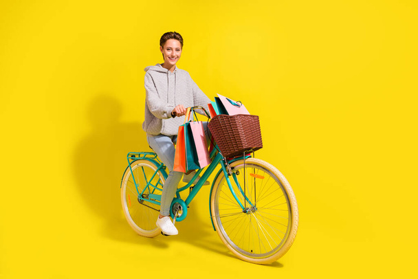 Full body photo of crazy brown hair millennial lady ride bicecly with bags wear sweater jeans sneakers isolated on yellow background. - Foto, imagen