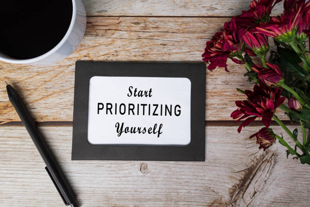 Motivationeel citaat op schoolbordlijst en witte bloemen op houten bureau - Beginnen met het prioriteren van uzelf. - Foto, afbeelding