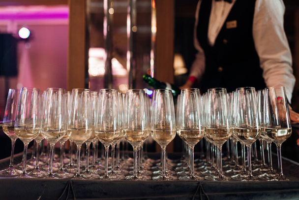 Ober serveert rij glazen witte champagne op dienblad in restaurant close-up. Mousserende wijn in glazen gieten, feest vieren. Banketzaal, feestelijk diner, luxe service. - Foto, afbeelding