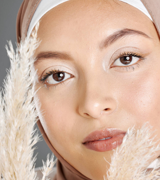 Zbliżenie portret twarz pięknej młodej muzułmanki noszącej naturalny makijaż i chusta pozowanie z roślin pszenicy pampas na tle studio. Świecący, skromny arabczyk pokryty tradycyjnym hidżabem. - Zdjęcie, obraz