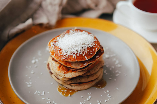 Banana Pancakes with maple syrup and coconut flakes and cup of tea for breakfast on table - Foto, Bild