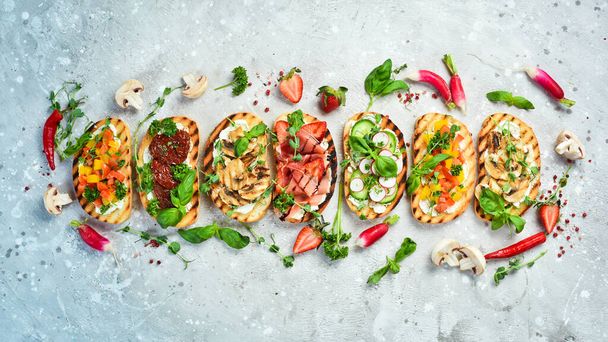 Delicious homemade bruschettas with vegetables, cheese, mushrooms and prosciutto. Sandwich. On a stone background. Top view. - Foto, afbeelding