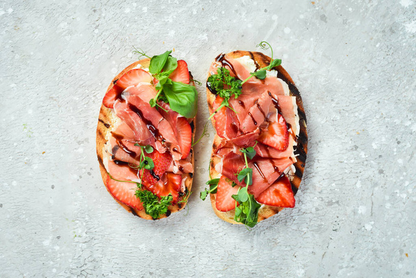Sandwich with cheese, prosciutto, strawberries and basil. Bruschetta. Top view. On a stone background. - Fotografie, Obrázek