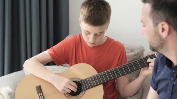 Syn gra na gitarze, ojciec i siostra słuchają melodii. Nastoletni chłopak grający na gitarze w rodzinnym kręgu - Materiał filmowy, wideo