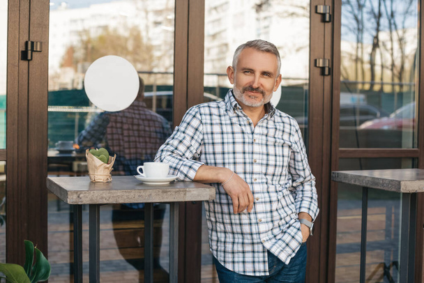 All excellent. Attractive smiling middle aged man looking confidently at camera standing with his back to cafe outdoor - 写真・画像