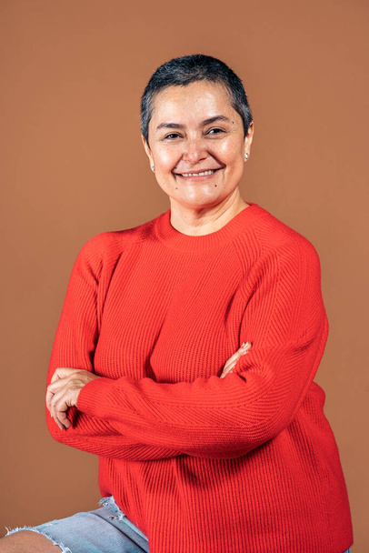Stock photo of smiley woman with short grey hair posing in studio shot against brown background. - Zdjęcie, obraz