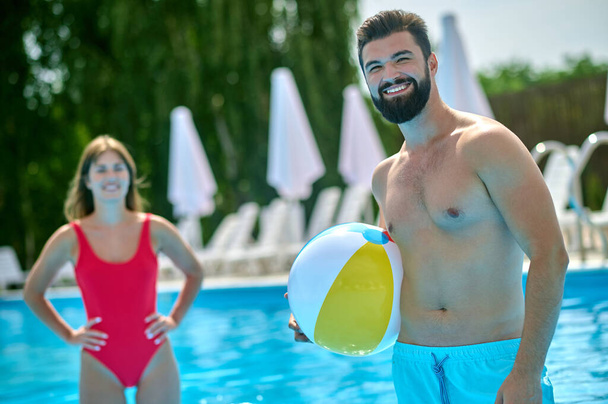 Cheerful fit young man with the game ball in the hand standing in the water beside a smiling female - Foto, Imagen