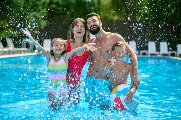 Happy modern young parents and their cute joyous children standing in the outdoor swimming pool - Фото, зображення