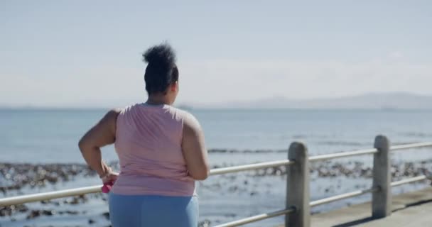 One plus size woman running with dumbbells to get fit outdoors from the back. Determined to reach weightloss goal for better health and wellbeing. Overweight woman doing cardio training exercise. - Πλάνα, βίντεο
