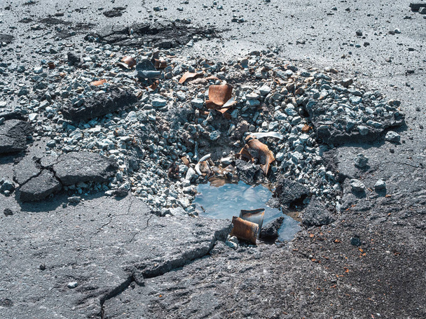 Guerre en Ukraine, un cratère dans l'asphalte d'une coquille, l'eau sort de l'entonnoir d'une coquille - Photo, image