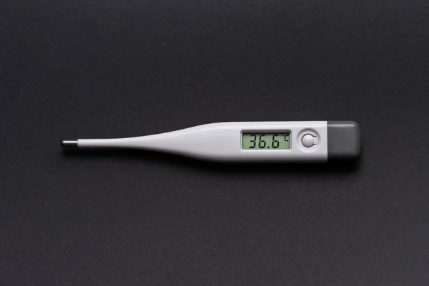 белый электронный термометр показывает нормальную температуру тела на черном фоне - Фото, изображение