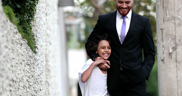 Hermoso padre e hijo de raza mixta caminando juntos en la acera urbana de la ciudad, padres y vínculos étnicamente diversos con jóvenes - Foto, Imagen