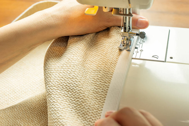 Seamstress hands holding white textile fabric. Female hands stitching white fabric on modern sewing machine at workplace. Close up view of sewing process. Handmade, hobby, small business concept - Photo, Image