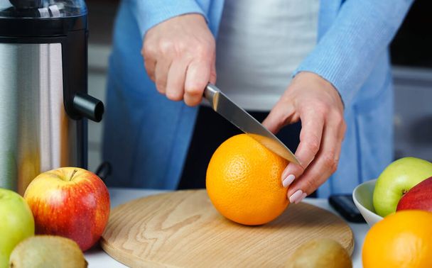 Die Hände der jungen Frau schneiden mit einem Messer eine Orange, um in der Küche frischen Saft herzustellen. Gesunde oder diätetische Ernährung Konzept. Nahaufnahme. - Foto, Bild