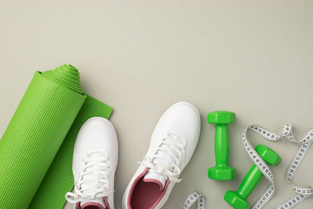 Fitness konsepti. Dambılların, beyaz spor ayakkabıları ve yeşil spor minderlerinin izole edilmiş pastel arka plandaki halterlerin en üstteki fotoğrafı. - Fotoğraf, Görsel
