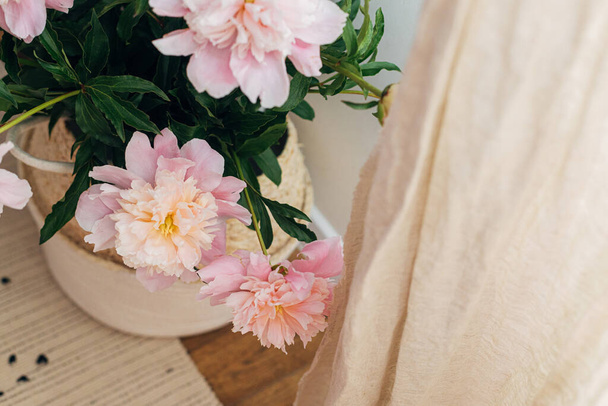 美しい牡丹の花束のバスケットリネンカーテンの近くのブーブールームです。モダンなボヘミアン装飾、スタイリッシュな快適なインテリアの詳細。素朴な背景に優しいピンクの牡丹の花、大気中のイメージ - 写真・画像