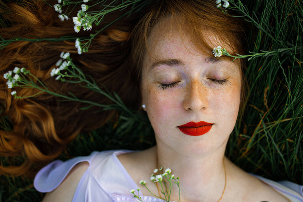 gyönyörű fiatal lány hosszú vörös göndör hajjal. Hajhullám hever a zöld fűben. felülnézetből - Fotó, kép