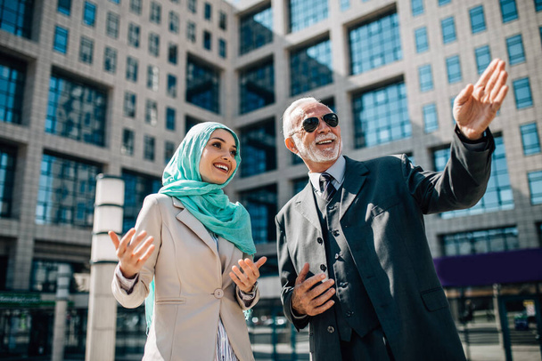 Young beautiful muslim woman with hijab standing in front of modern city building and talking with senior business man. Global investment business concept. - Foto, imagen