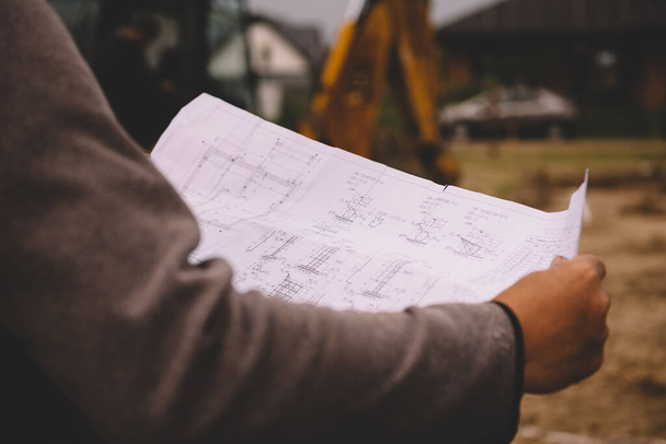 Architect showing house build plans at the building site. Engineer working with blueprints outside on construction site - Фото, зображення