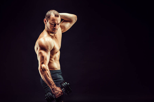 Powerful man doing the exercises with dumbbells. Photo of young man with good physique isolated on black background. Strength and motivation.  - Zdjęcie, obraz