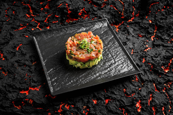 Raw tuna, avocado onion salad served in culinary ring on black plate. Black  background. Tartar - Фото, зображення