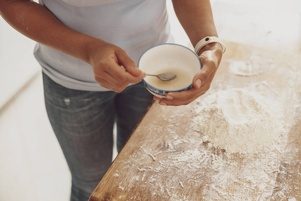 Les mains des femmes tiennent un bol avec oeuf pour ajouter à la pâte à pizza sur le fond de la planche de cuisine - Photo, image