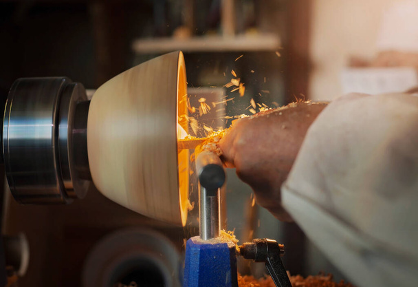Una ciotola di legno girata da un uomo su un tornio per la tornitura del legno.Un artigiano al lavoro.La segatura vola. - Foto, immagini