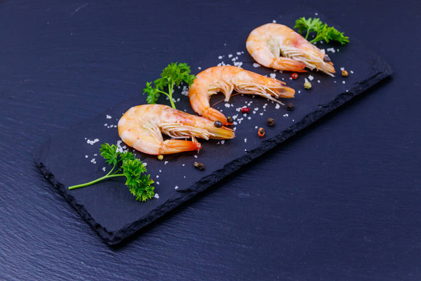 Big raw red prawns with parsley, salt and pepper on a slate board on black background - Foto, immagini