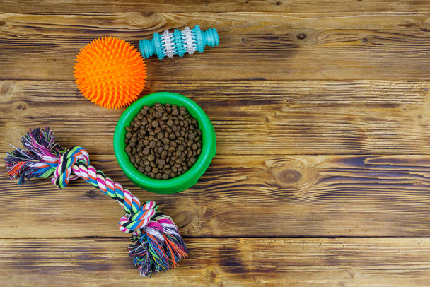 Dog toys and feed for dogs in green plastic bowl on wooden background. Dog care concept - Fotoğraf, Görsel