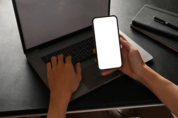 Pracownik biurowy lub biznesmen szukający informacji na ekranie smartfona i wpisujący zawartość na przenośnym laptopie. obraz z bliska - Zdjęcie, obraz