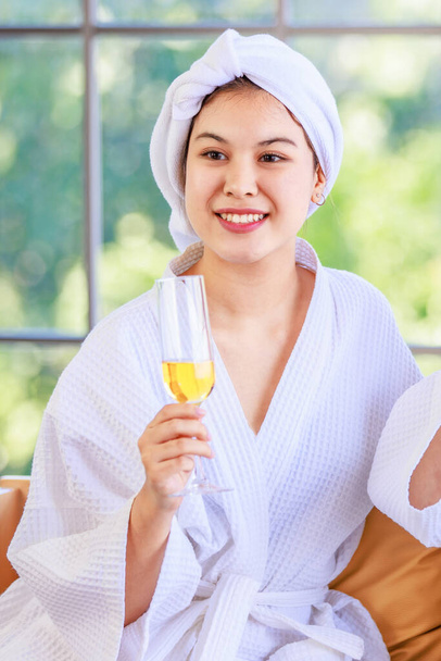 Asian young beautiful spa customers friend in white clean bathrobe covered head with towel sitting smiling holding drinking fruit juice beverage glasses talking together after therapy session. - Photo, Image