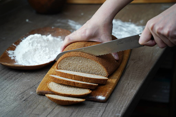 A woman cuts a loaf of bread on the table. - 写真・画像