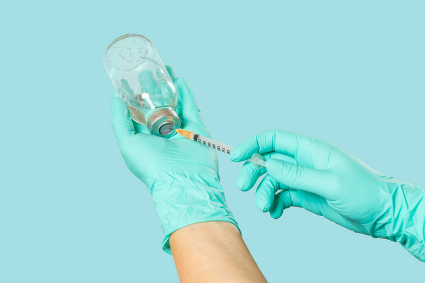 Frasco de vidrio para medicina líquida y una jeringa de plástico para inyección en las manos en guantes de látex sobre menta verde. - Foto, Imagen
