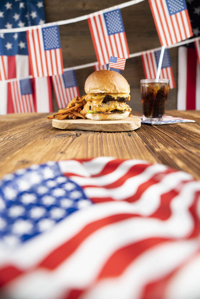 Celebración del 4 de julio. Bandera americana y decoraciones. Hamburguesas sobre mesa rústica de madera
. - Foto, imagen