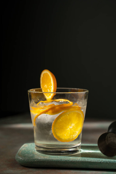 Bicchiere di gin tonic con fetta di arancia e ghiaccio, su un tavolo di pietra e sfondo verde scuro - Foto, immagini