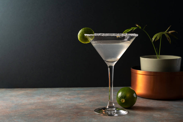 Aito margarita cocktail limetillä suolatussa vannetussa lasissa, maanläheisellä värillisellä pinnalla ja tyylikkäällä tummalla taustalla, herkullinen meksikolainen juoma tequilalla, sitruuna, karvas appelsiinilikööri, koristeltu saalilla - Valokuva, kuva