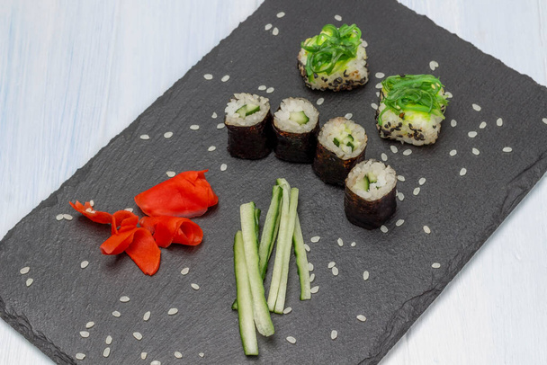 Sushi nori and sushi with seaweed, sliced cucumber and pickled ginger on stone board. Top view. White background. - Photo, Image