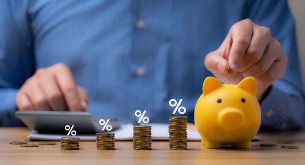 pile of coins and piggy bank, Interest rate and dividend concept Businessman is calculating income and return on investment in percentage. income, return, retirement, compensation fund, investment - Photo, image