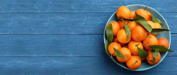 Fresh ripe tangerines and green leaves on blue wooden table, top view with space for text. Banner design - Zdjęcie, obraz