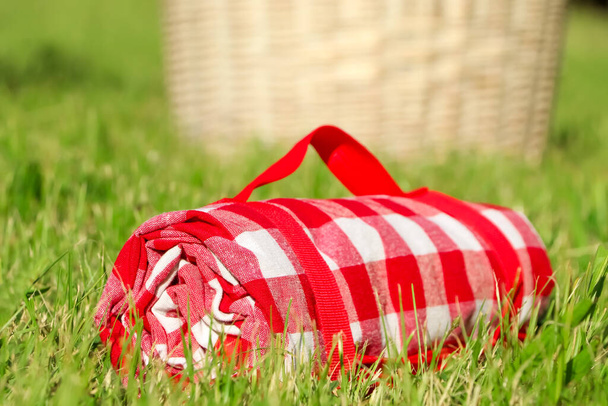 Rolled checkered picnic tablecloth on green grass, closeup - Fotoğraf, Görsel