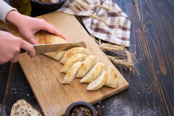 Woman cutting freshly baked bread at wooden kitchen table. - Фото, зображення