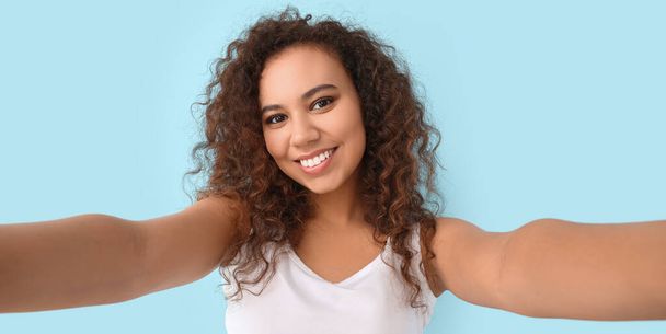 Schöne junge Afroamerikanerin macht Selfie auf hellblauem Hintergrund - Foto, Bild