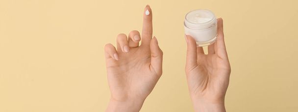 Hands of young woman with cosmetic cream on beige background - Photo, Image
