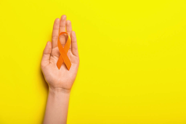Woman with orange awareness ribbon on yellow background. Kidney cancer concept - Φωτογραφία, εικόνα
